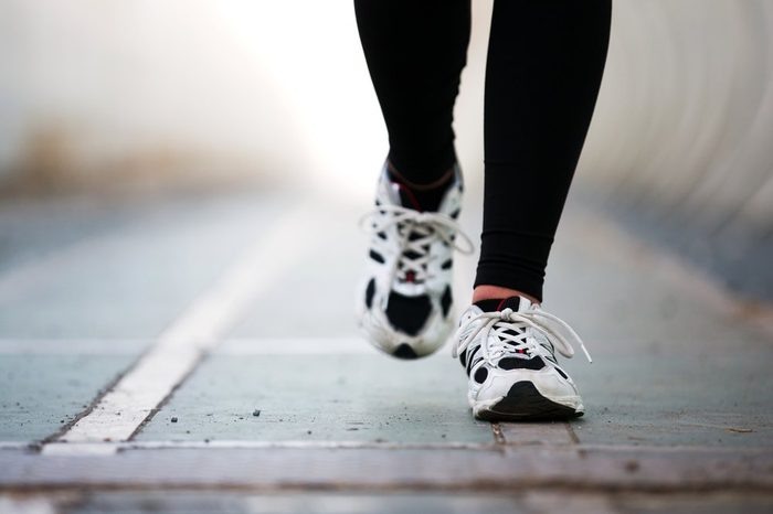 Runner feet walking on road closeup on shoe. woman fitness jog workout wellness concept.