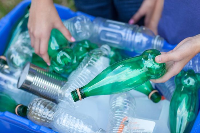 Caucasian boy and girl putting clear and green bottles and metal cans in recycling blue bin outside in yard