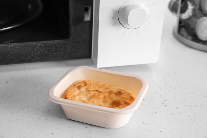 Container of cottage cheese casserole near microwave on table