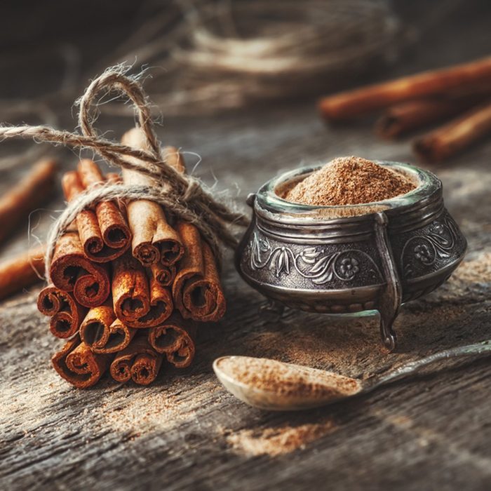 Ground cinnamon, cinnamon sticks, tied with jute rope on old wooden background in rustic style