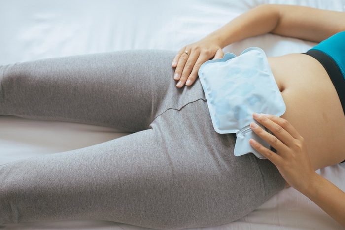 Woman holding hot water bag on her stomach in bedroom,Female lying in bed with dysmenorrhea