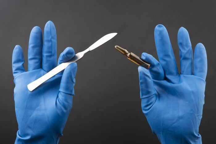 Medical scalpel and vial for injection in hands wearing blue gloves