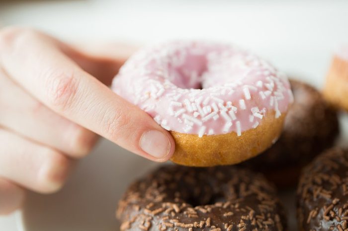 people, food, junk-food and eating concept - close up of female hand holding glazed donut