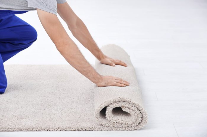 Male worker unrolling carpet indoors