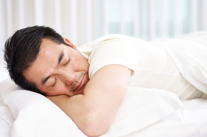 asian man lying on front in bed sleeping.
