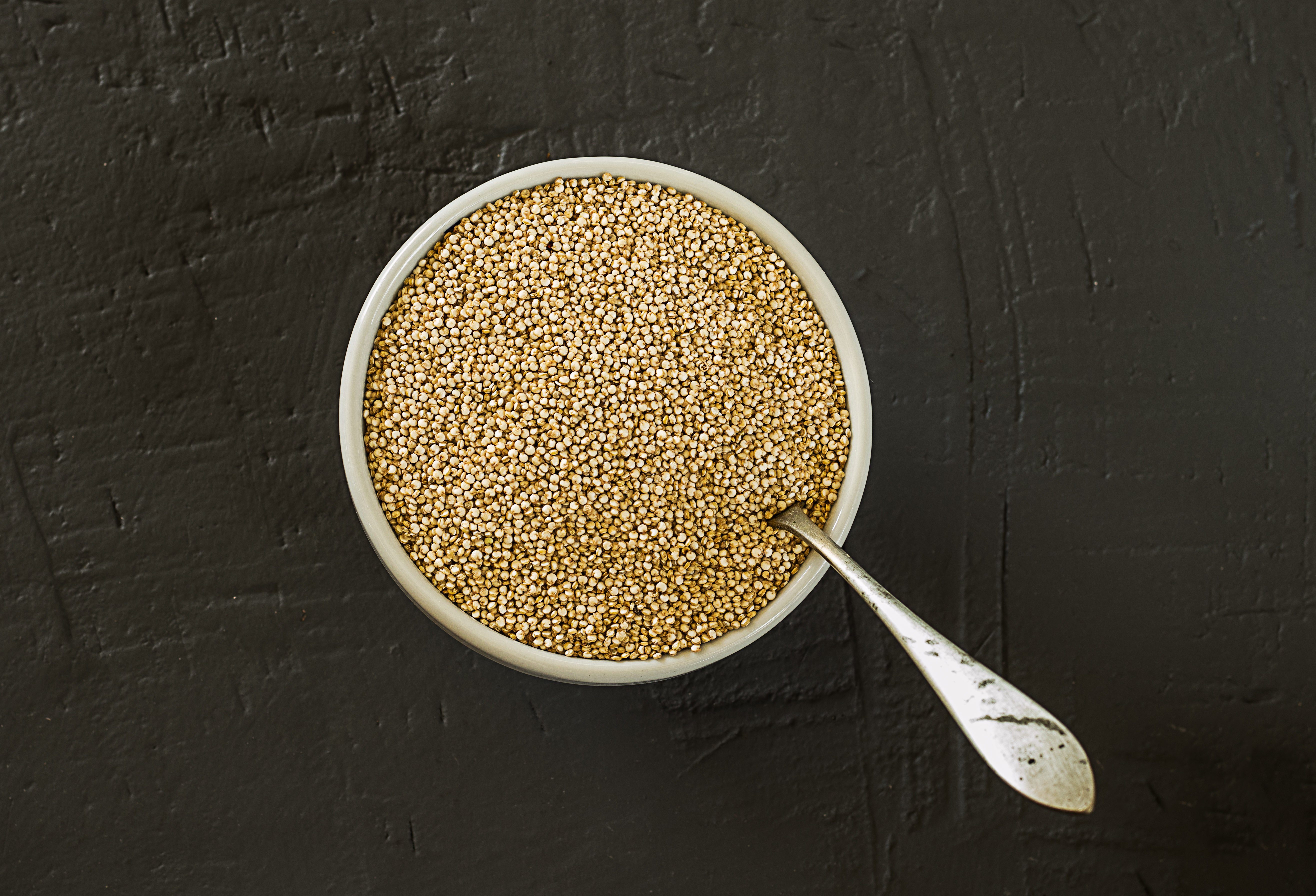 Quinoa seeds in a bowl and spoon. Healthy, protein-rich carbohydrates. Rustic and dark background