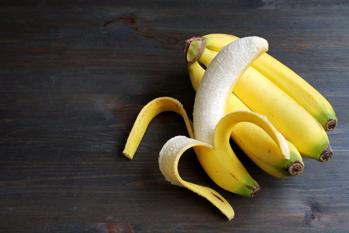One peeled banana on a bunch of bananas isolated on dark brown wooden table with copy space