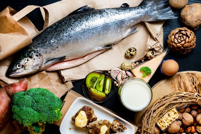 Products containing phosphorus salmon fish, pine nuts, peanuts, anchovy, cheese, milk, eggs, broccoli, kiwi, potatoes, meat, beans garlic on a round cutting board and black wooden background