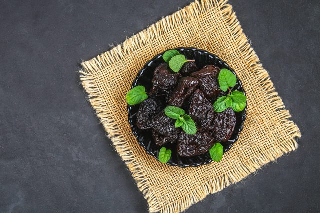 Prunes and fresh mint leaves in a bowl on a concrete table.