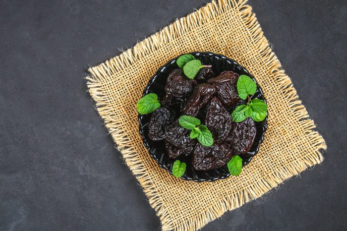 Prunes and fresh mint leaves in a bowl on a concrete table.