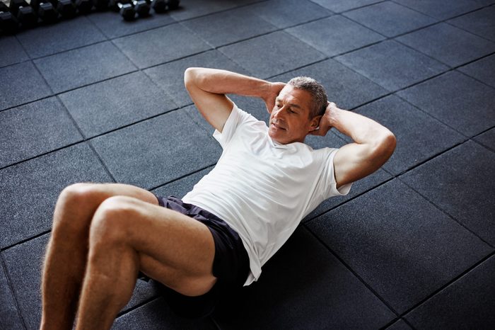 Focused senior man in sportswear doing sit ups alone while working out on the floor of a gym