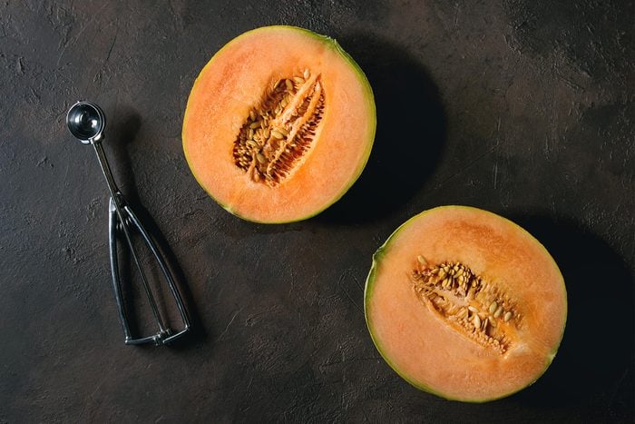 Half of ripe organic Cantaloupe melon with seeds and spoon over dark brown texture background. Flat lay, space