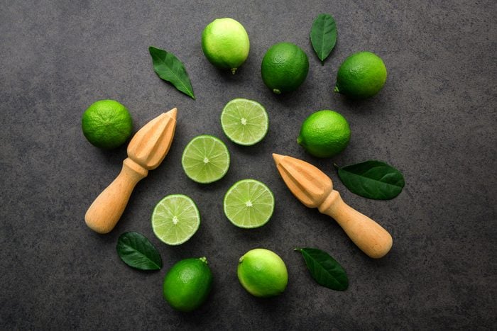 Fresh limes and wooden juicer on dark background. Top view with copy space