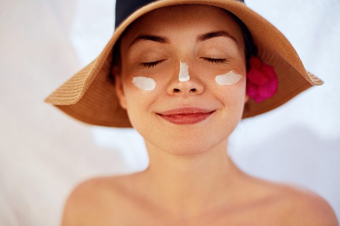 Woman smile applying sun cream on face. Skincare. Body Sun protection. sunscreen. Female in hat smear moisturizing lotion on skin.