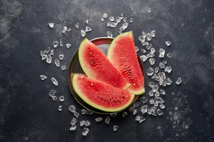 Slices of red watermelon and ice cubes on dark background, top view