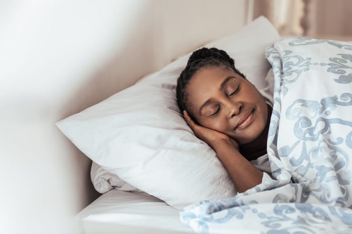 Content young African woman sleeping peacfully under a duvet in her bed at home in the early morning