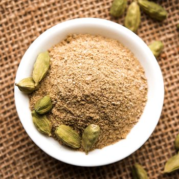 elaichi or Cardamom powder in bowl or heap over moody background with pods.