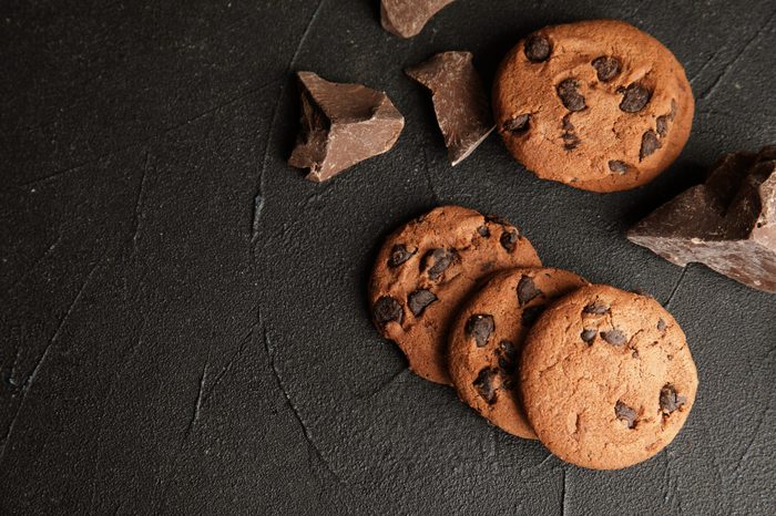 Tasty chocolate chip cookies on dark background, flat lay. Space for text