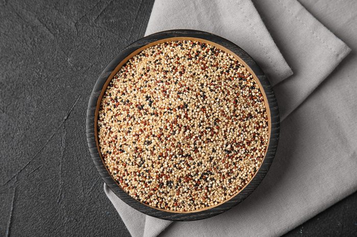Plate with mixed quinoa seeds on dark background, top view