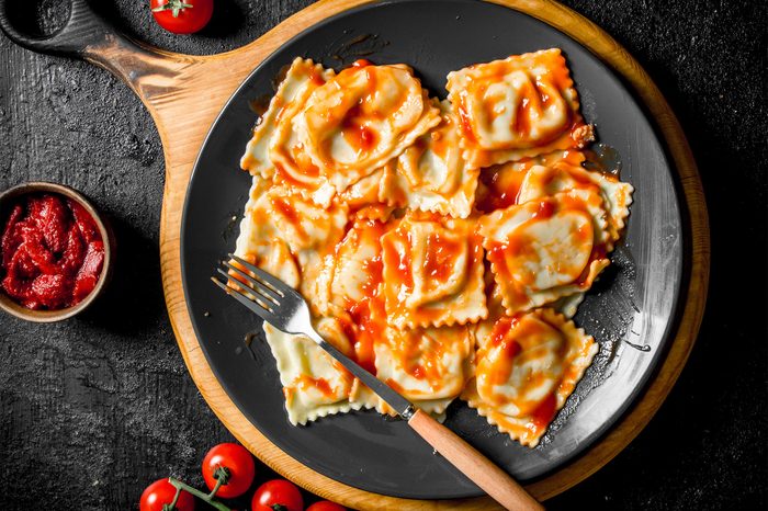 Ravioli with veal and tomato sauce. On black rustic background