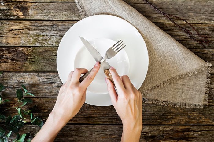 Restaurant and food theme: human hands show on a wooden background. Healthy food theme: hands holding knife and fork on a plate, top view