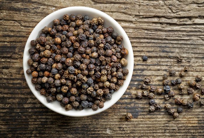 Bowl of black pepper on old wooden table