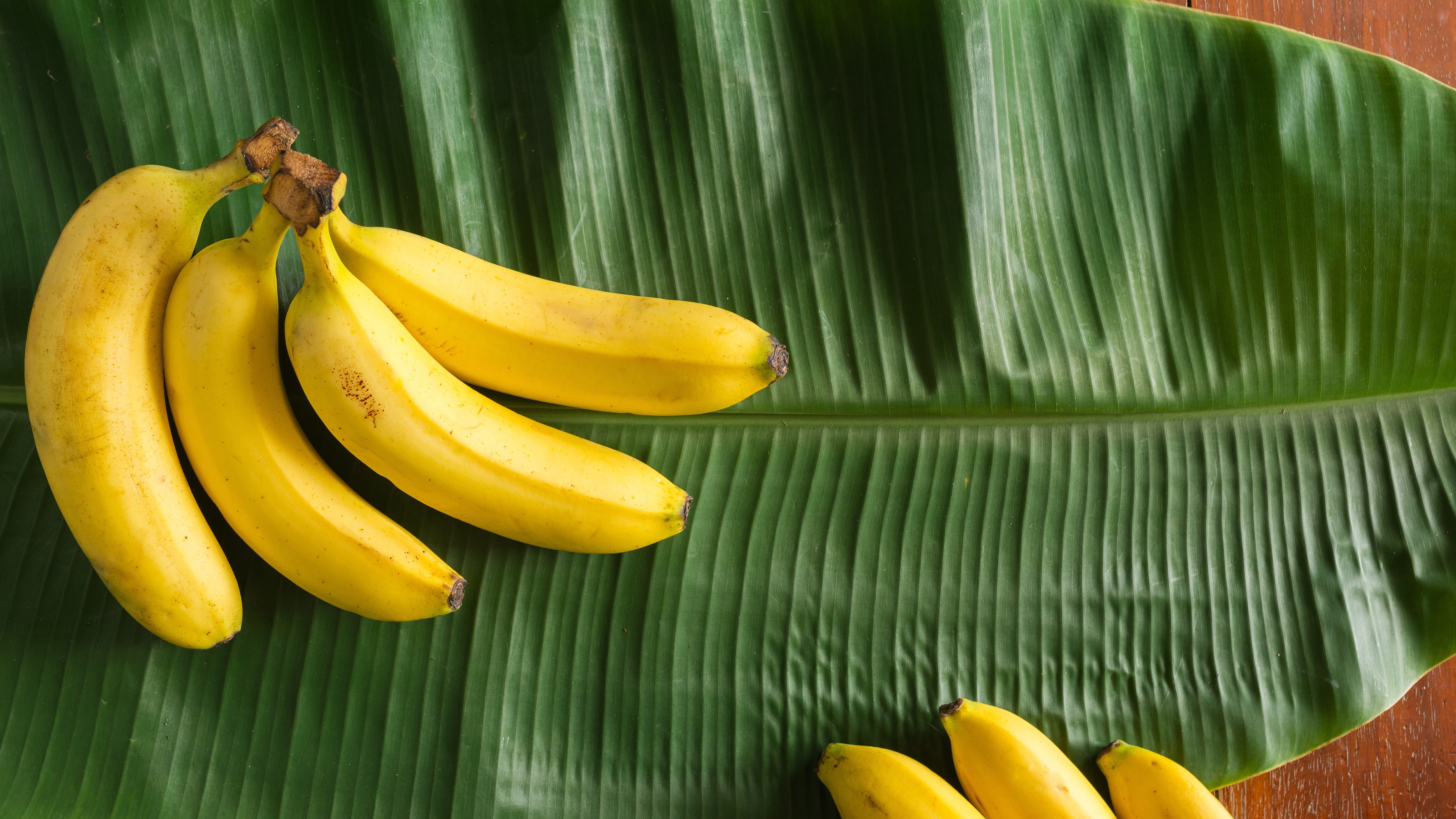 a pile of yellow bananas lay on top of the green fresh banana leaf