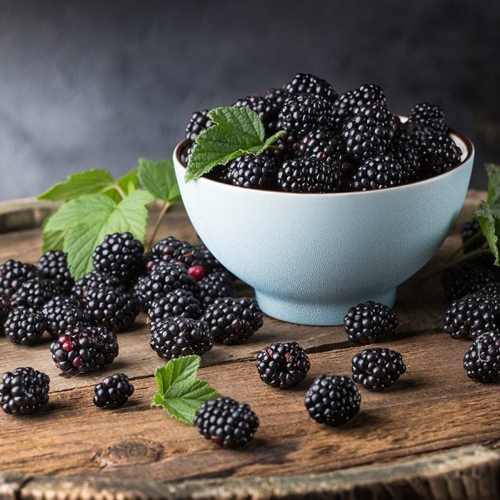 Ripe blackberries with leaves in a bowl on a wooden board on a dark background