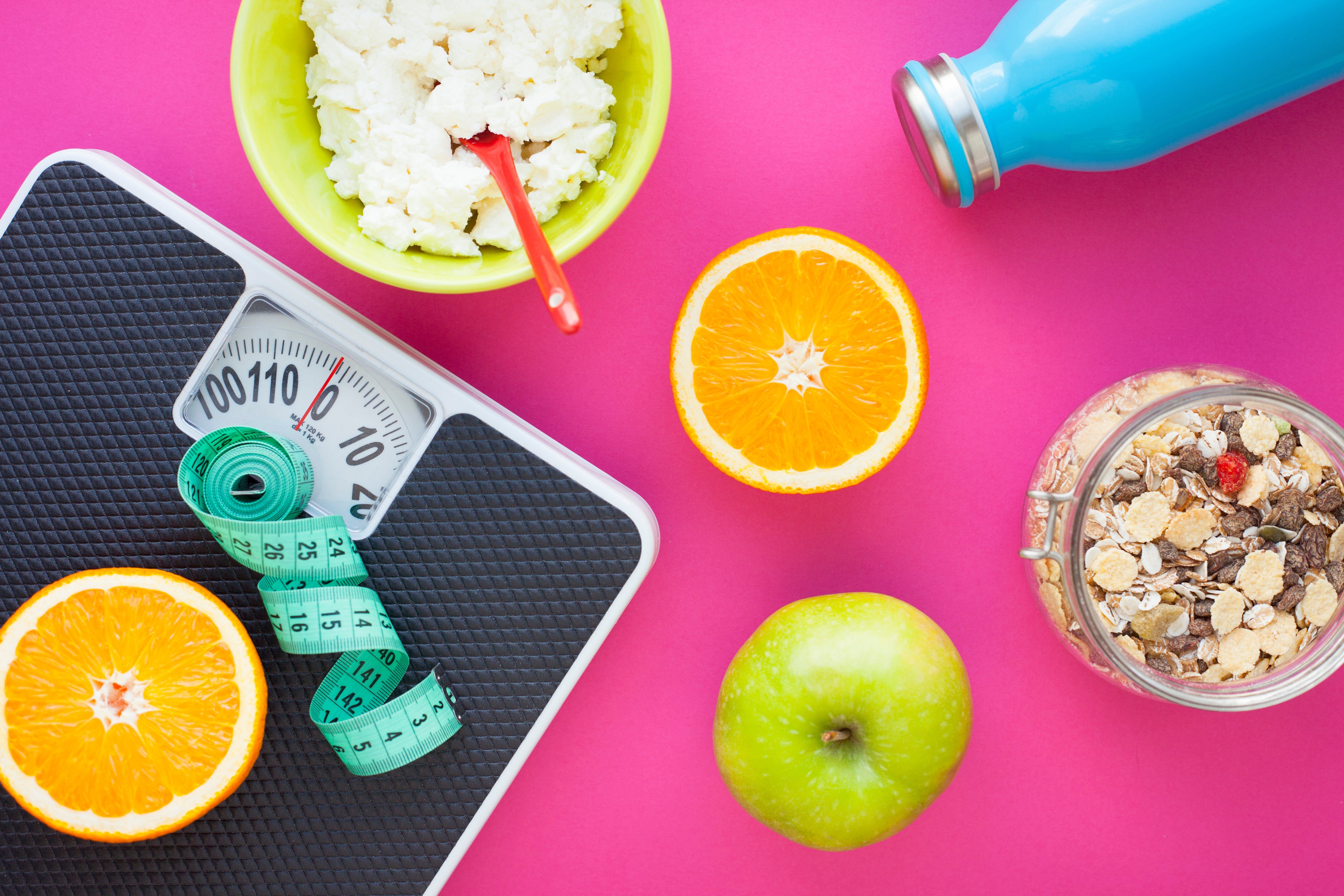 Fruits, curd, measuring tape, water and muesli on the pink background. Weight loss, diet controlled healthy food concept background. Top view, close up.