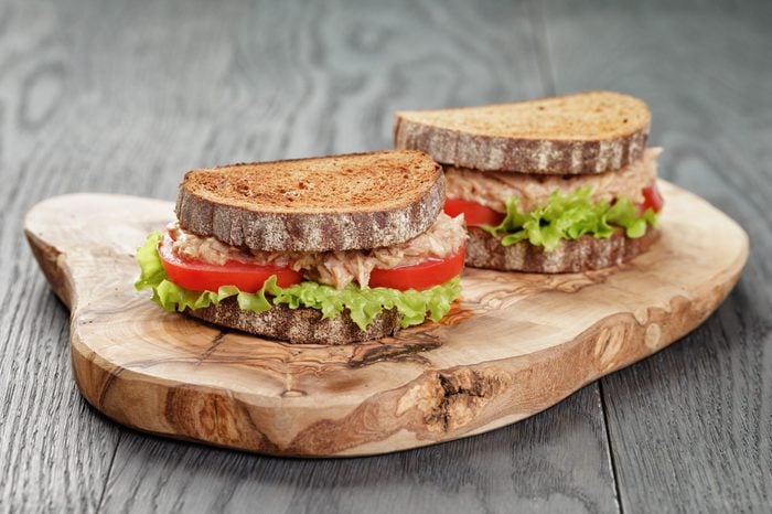 rye bread sandwich with tuna and vegetables on wood background