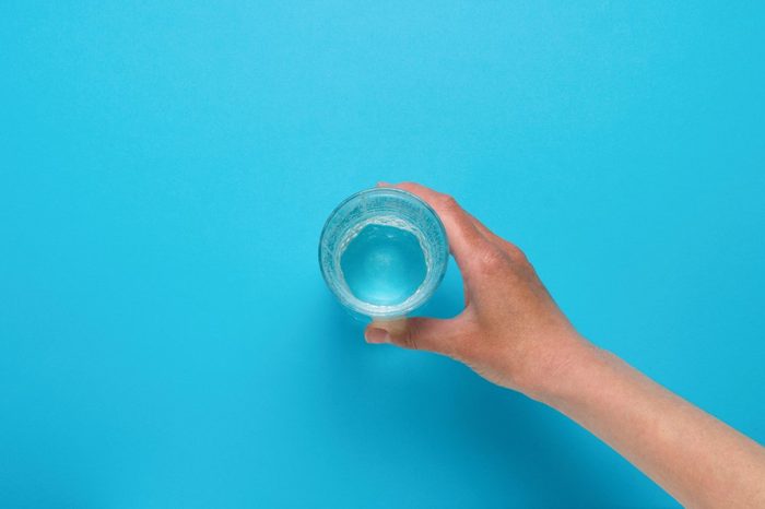 Female hand taking a glass of water on a blue background. Flat Lay Still Life Table Top View Blue Background.