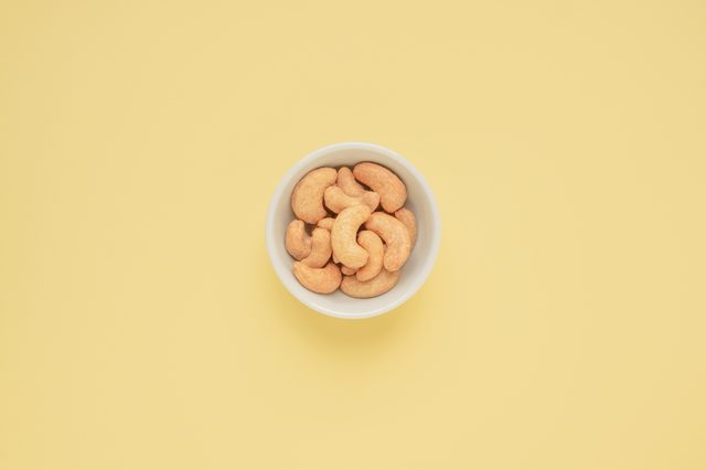 Cashew nuts in white cup on yellow background and copy space, Top view, Color pastel style