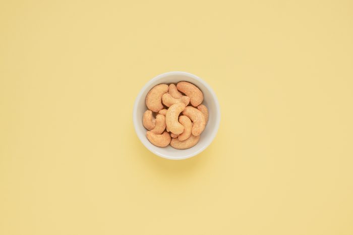 Cashew nuts in white cup on yellow background and copy space, Top view, Color pastel style