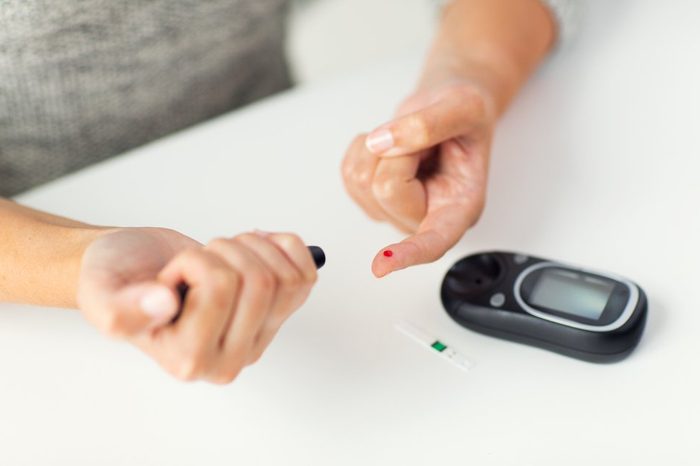 medicine, diabetes, glycemia, health care and people concept - close up of woman checking blood sugar level by glucometer at home