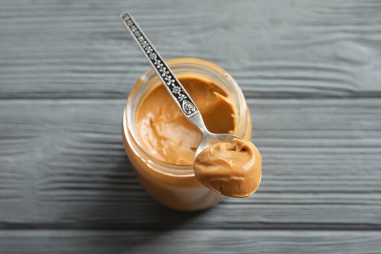 Spoon and glass jar with creamy peanut butter on wooden background