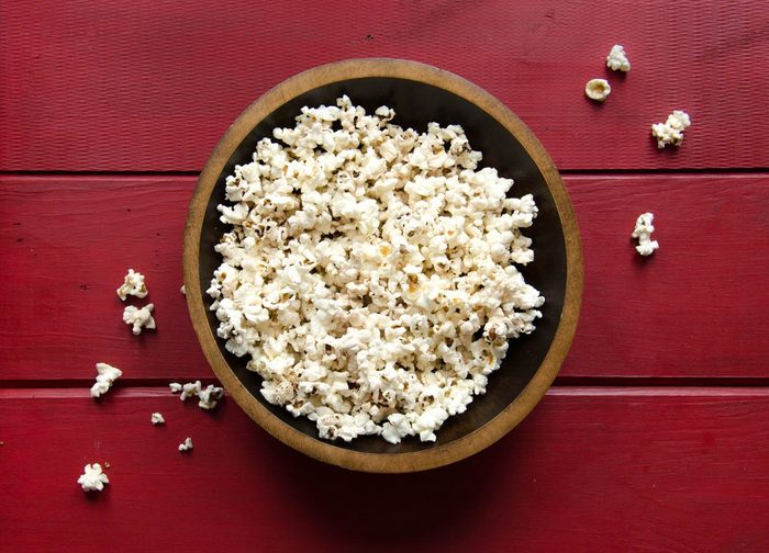 Bowl of popcorn in wooden bowl on red wood background