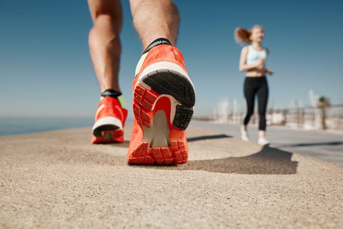 Runner feet running on road closeup on shoe. Sportsman fitness sunrise jog workout welness concept.