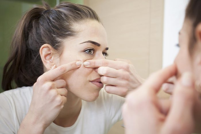 woman looking in the mirror and squeezing a pimple 