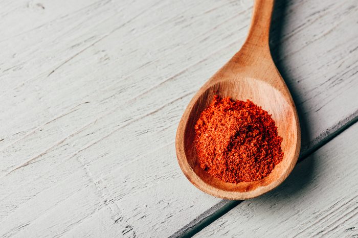 Spoonful of red chili pepper powder in a wooden spoon on a white wooden table.