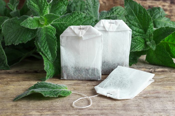 White packages of disposable tea with mint branches on a wooden tabletop.