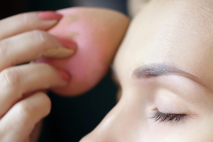 A woman applying foundation to her forehead with a pink beauty blender. | These skin care ingredients can cause breakouts.