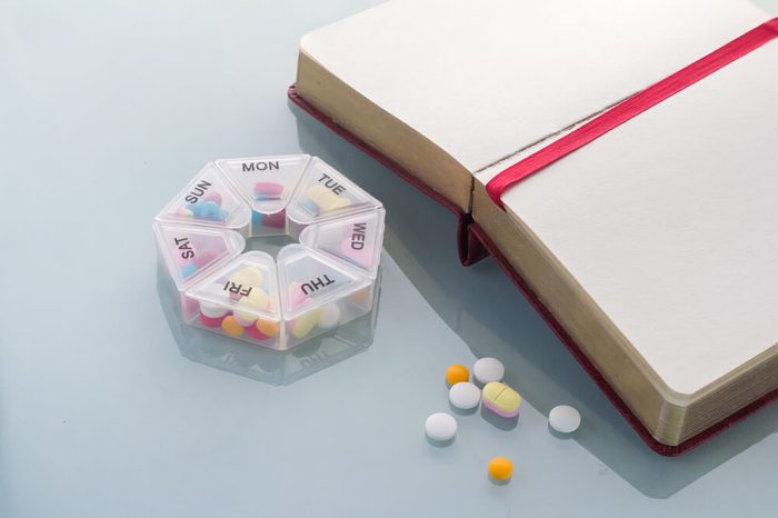 Pills planner with weekly medication capsules in it with notebook on glass top table