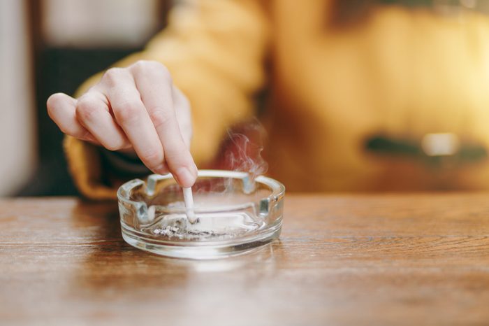 Focus on caucasian young woman hand putting out cigarette on glass ashtray on wooden table, cigarette butt, smoking is dying. Quit smoking. Health concept. Close up photo