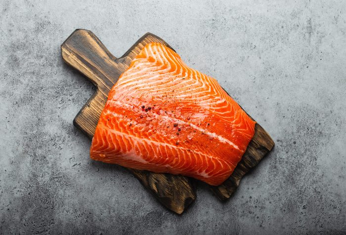 build muscle | fresh raw salmon fillet with seasonings on wooden board, gray stone background. Preparing salmon fillet for cooking, healthy eating concept 