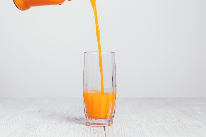 Orange juice is poured from a bottle into a glass on a white background