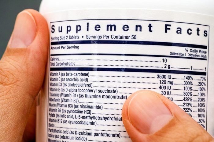 Close-up of white plastic jar with supplement facts of multivitamins in woman hands.