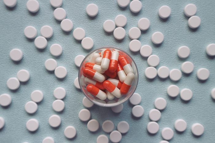 Orange capsule on bottle and white round pills on light blue table, healthcare 