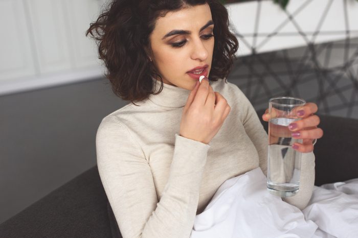 sick woman taking pill and holding glass of water at home