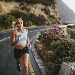 Fitness woman running on highway around the mountains. Female athlete training outdoors during rain.