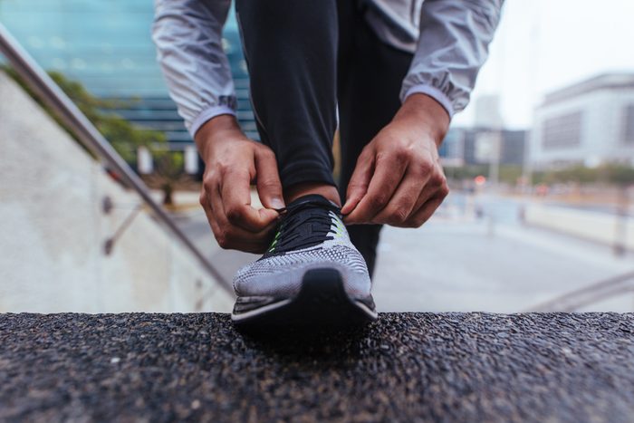 Male runner tying shoe lace on the steps of a building. Closeup of an athlete wearing running shoe.